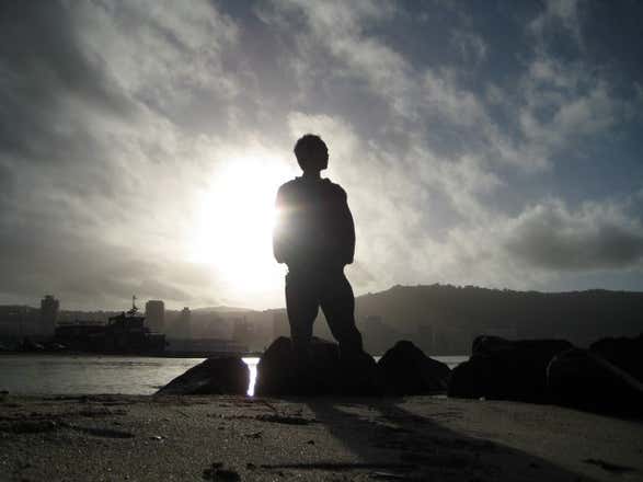 Man silhouette on rocky beach against sun 640x480